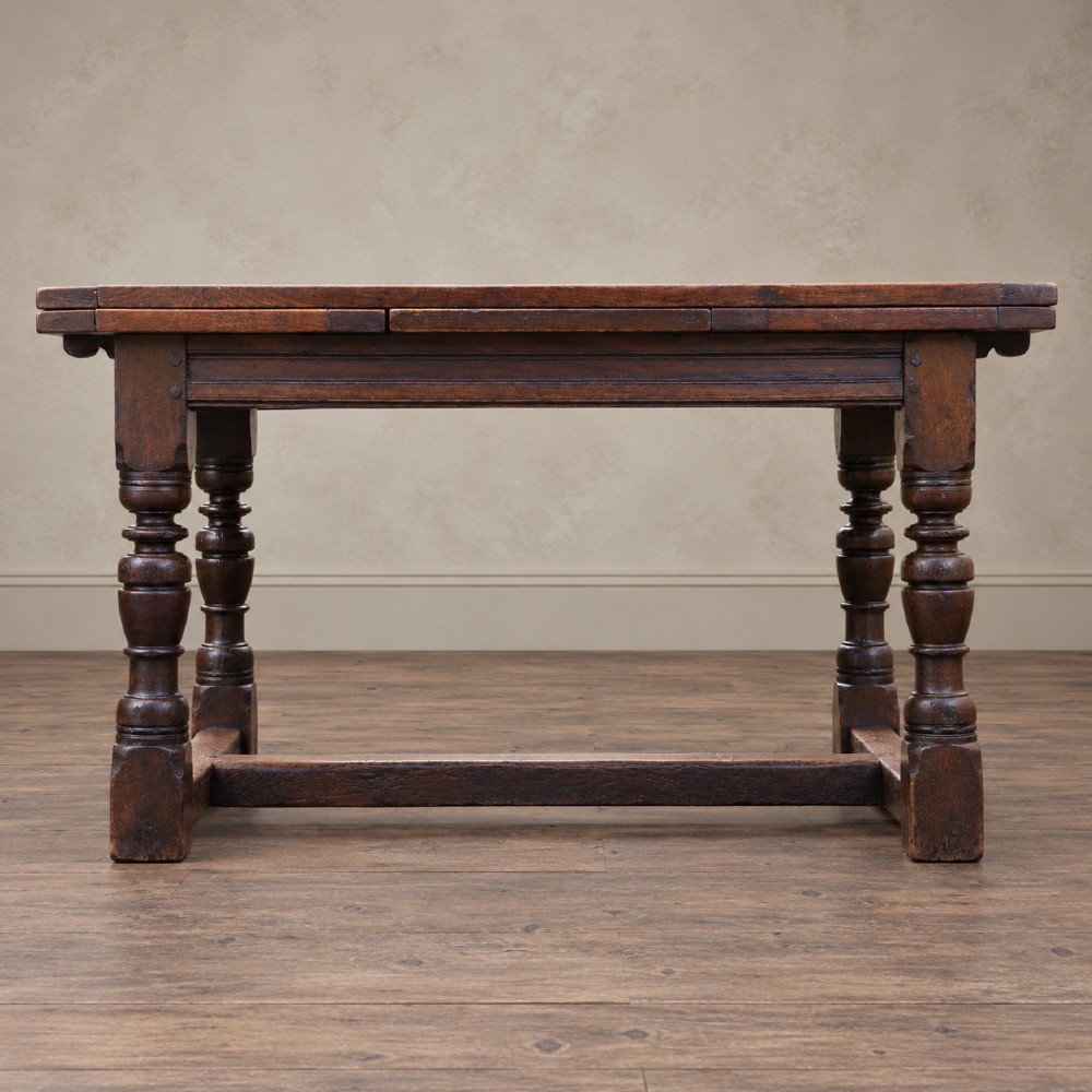A 17th-century solid oak extending dining table featuring turned legs, lower stretcher rails, and two draw-out end leaves. View II