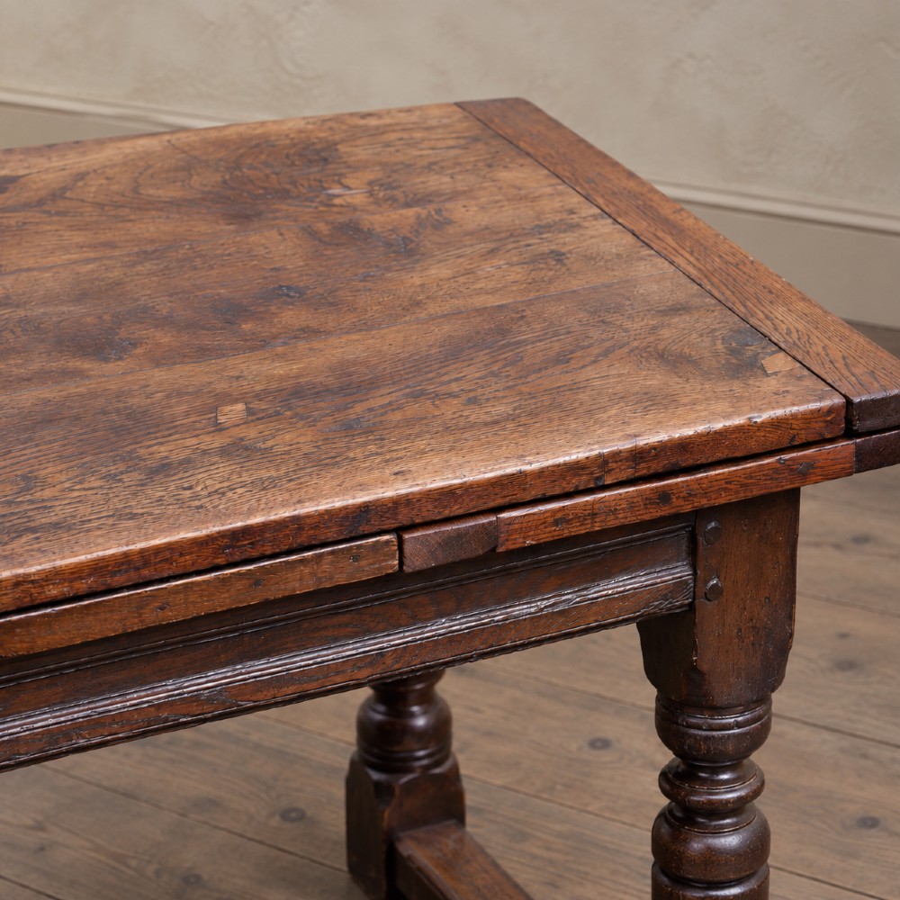 A 17th-century solid oak extending dining table featuring turned legs, lower stretcher rails, and two draw-out end leaves. View VI
