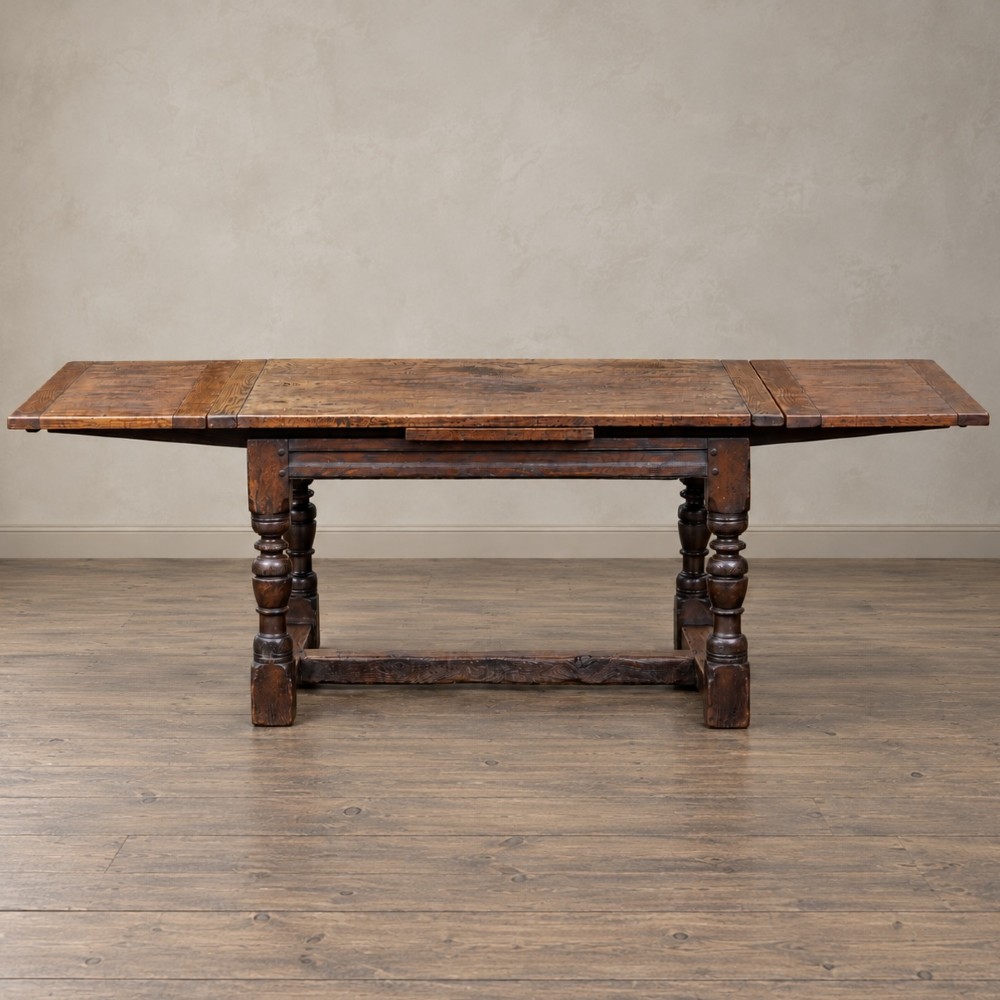 A 17th-century solid oak extending dining table featuring turned legs, lower stretcher rails, and two draw-out end leaves. View VII