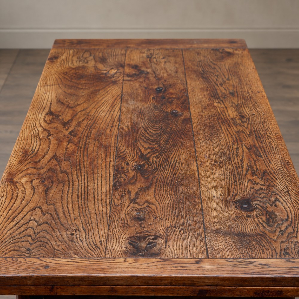 A 17th-century solid oak extending dining table featuring turned legs, lower stretcher rails, and two draw-out end leaves. View IX
