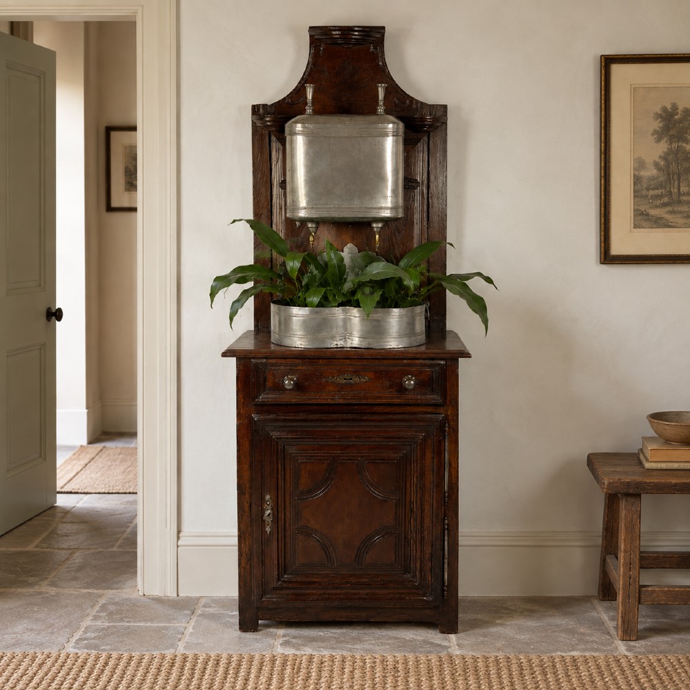 An 18th-century dark chestnut wood lavabo cabinet featuring a carved backboard mounted with a pewter cistern above a matching pewter basin.