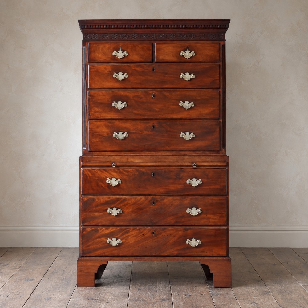 An eighteenth-century Georgian figured mahogany chest on chest featuring a carved dentil cornice, brass swan-neck handles, a pull-out brushing slide, and bracket feet.
