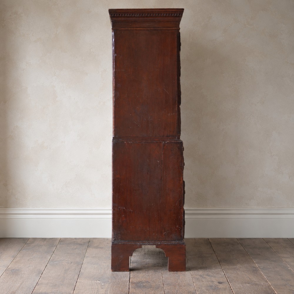 An eighteenth-century Georgian figured mahogany chest on chest featuring a carved dentil cornice, brass swan-neck handles, a pull-out brushing slide, and bracket feet. View V