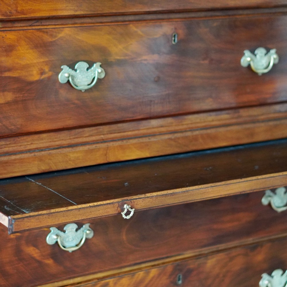 An eighteenth-century Georgian figured mahogany chest on chest featuring a carved dentil cornice, brass swan-neck handles, a pull-out brushing slide, and bracket feet. View VIII