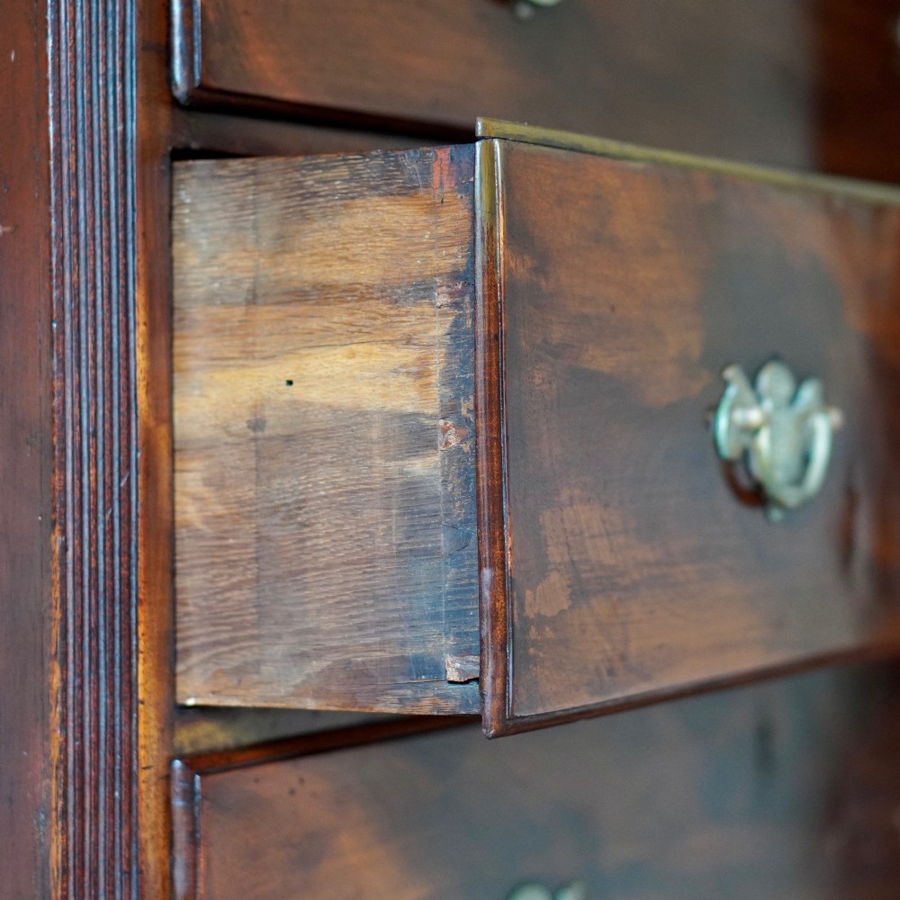 An eighteenth-century Georgian figured mahogany chest on chest featuring a carved dentil cornice, brass swan-neck handles, a pull-out brushing slide, and bracket feet. View XII
