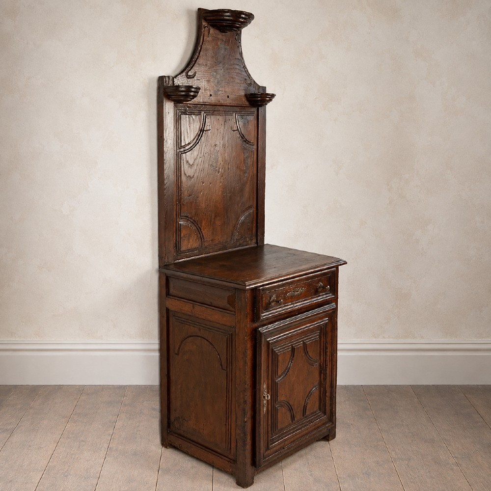 An 18th-century dark chestnut wood lavabo cabinet featuring a carved backboard mounted with a pewter cistern above a matching pewter basin. View VI