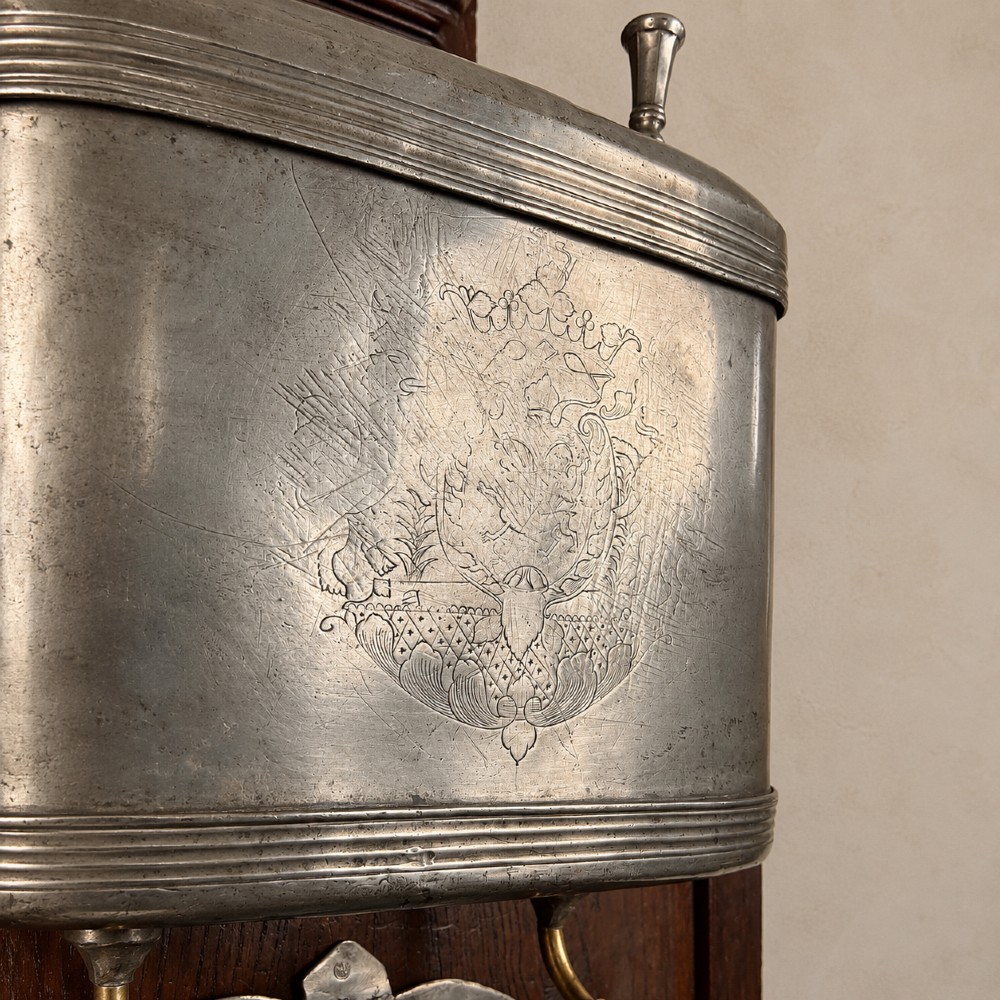 An 18th-century dark chestnut wood lavabo cabinet featuring a carved backboard mounted with a pewter cistern above a matching pewter basin. View XI