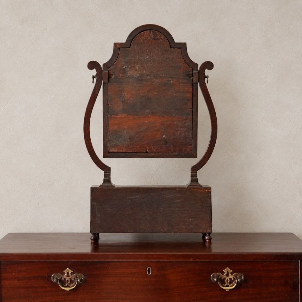 An antique Queen Anne walnut and laburnum toilet mirror featuring an arched cross-banded frame above a serpentine base with miniature drawers. View IV