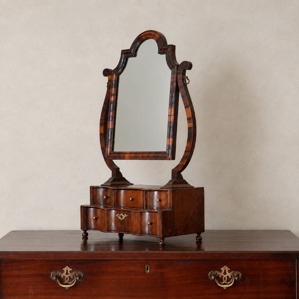 An antique Queen Anne walnut and laburnum toilet mirror featuring an arched cross-banded frame above a serpentine base with miniature drawers. View VI