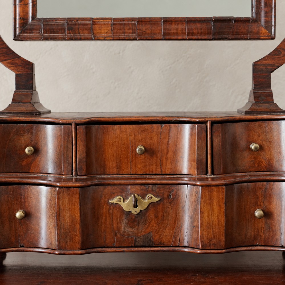 An antique Queen Anne walnut and laburnum toilet mirror featuring an arched cross-banded frame above a serpentine base with miniature drawers. View VII