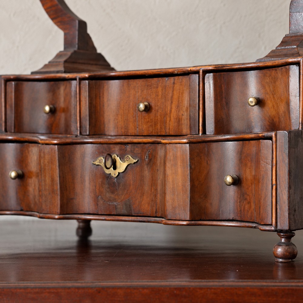 An antique Queen Anne walnut and laburnum toilet mirror featuring an arched cross-banded frame above a serpentine base with miniature drawers. View IX