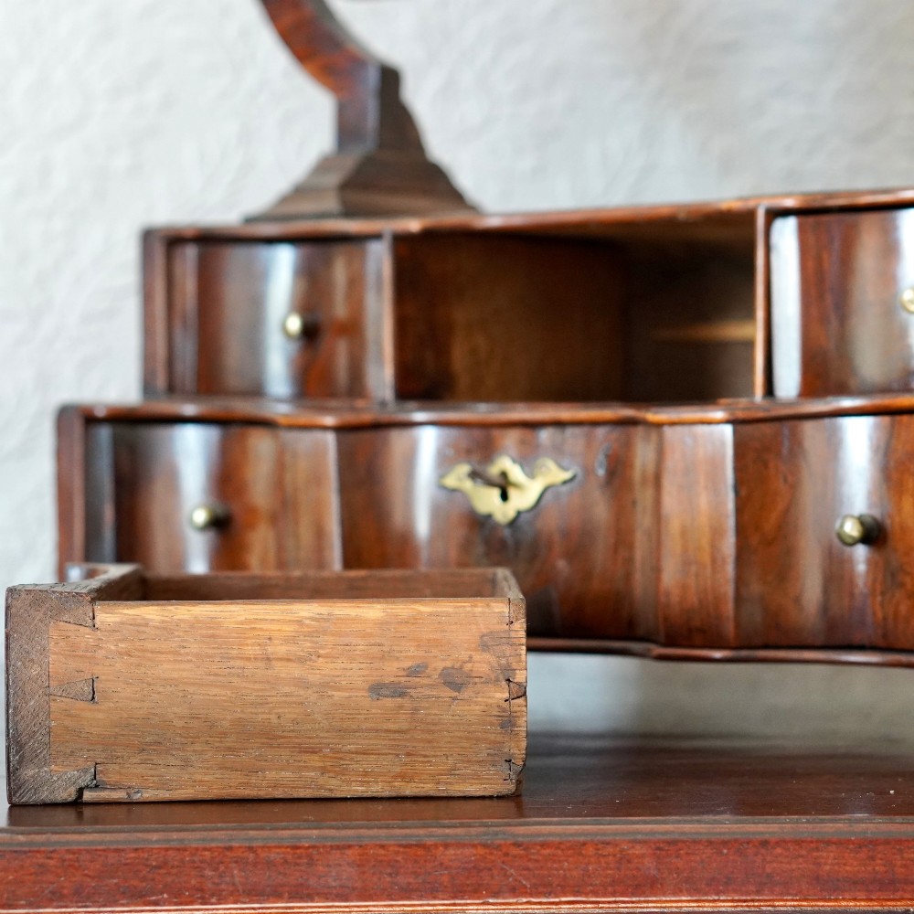 An antique Queen Anne walnut and laburnum toilet mirror featuring an arched cross-banded frame above a serpentine base with miniature drawers. View X