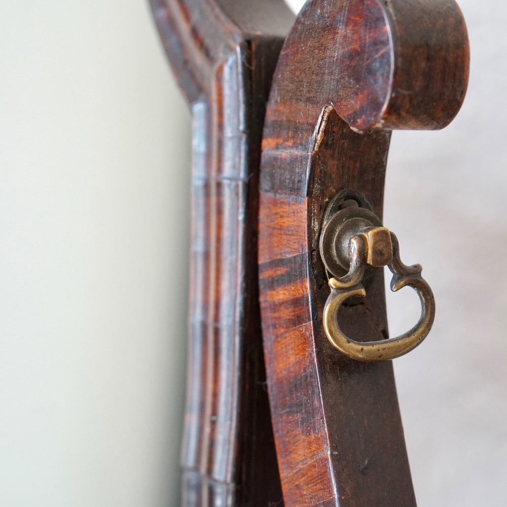 An antique Queen Anne walnut and laburnum toilet mirror featuring an arched cross-banded frame above a serpentine base with miniature drawers. View XV