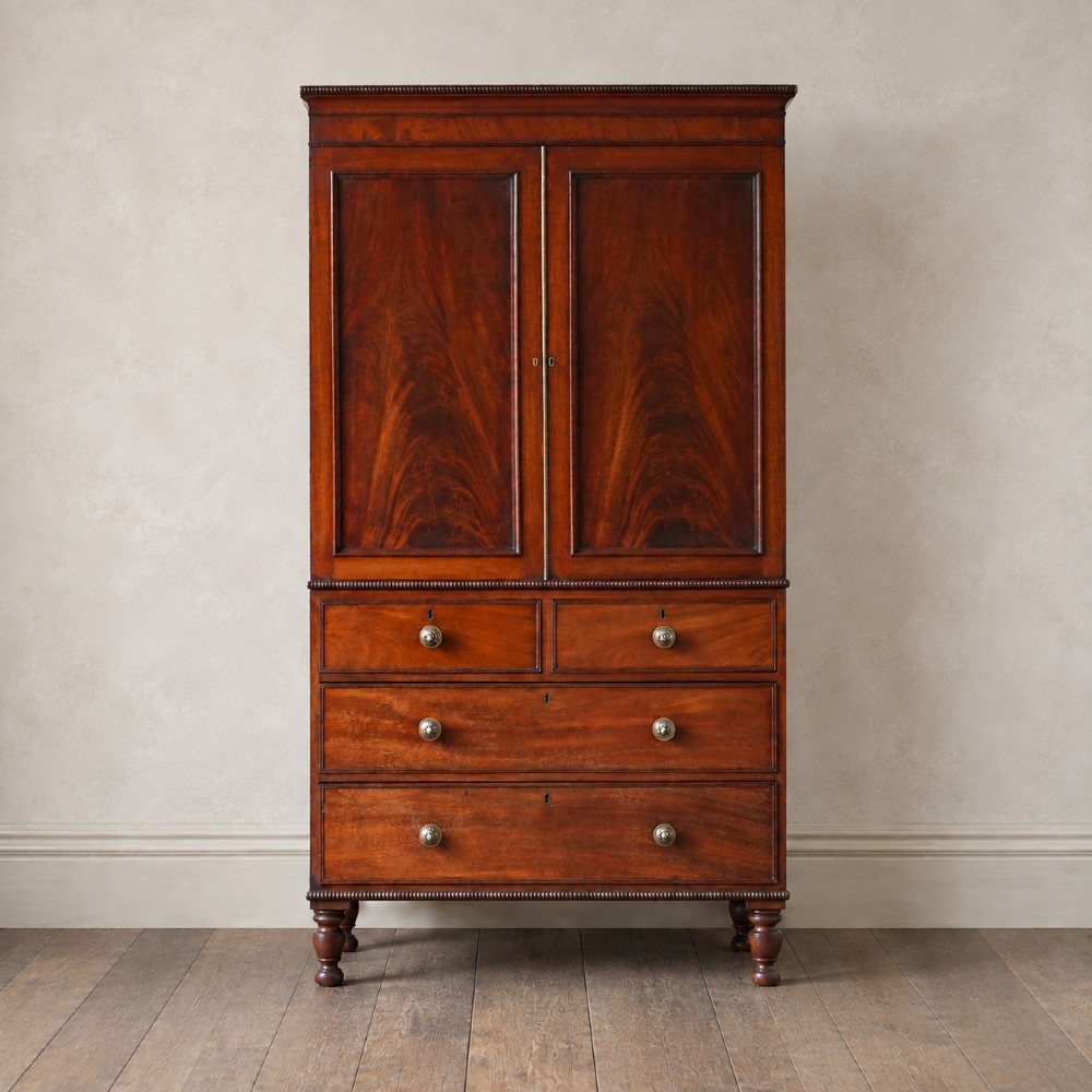 A Regency period flame mahogany linen press featuring a two-door upper cupboard above four drawers resting on turned legs.