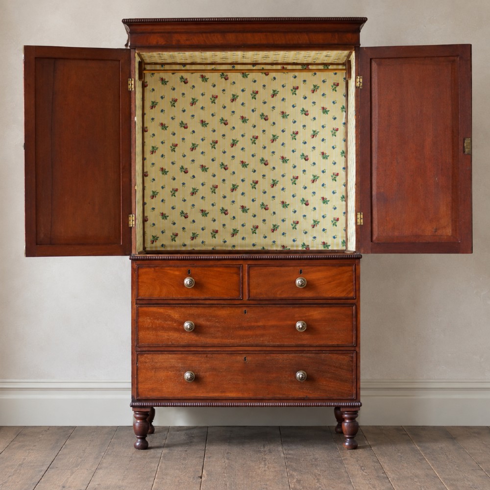 A Regency period flame mahogany linen press featuring a two-door upper cupboard above four drawers resting on turned legs. View II