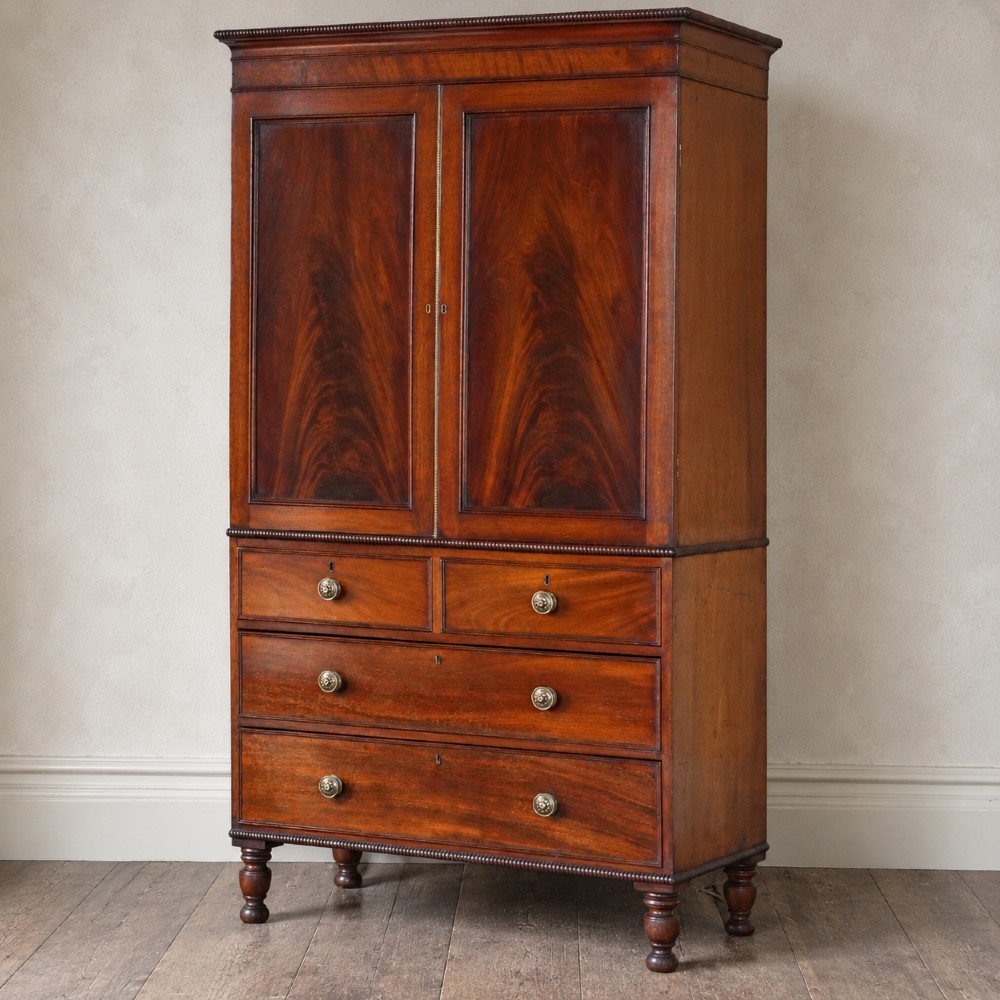A Regency period flame mahogany linen press featuring a two-door upper cupboard above four drawers resting on turned legs. View III