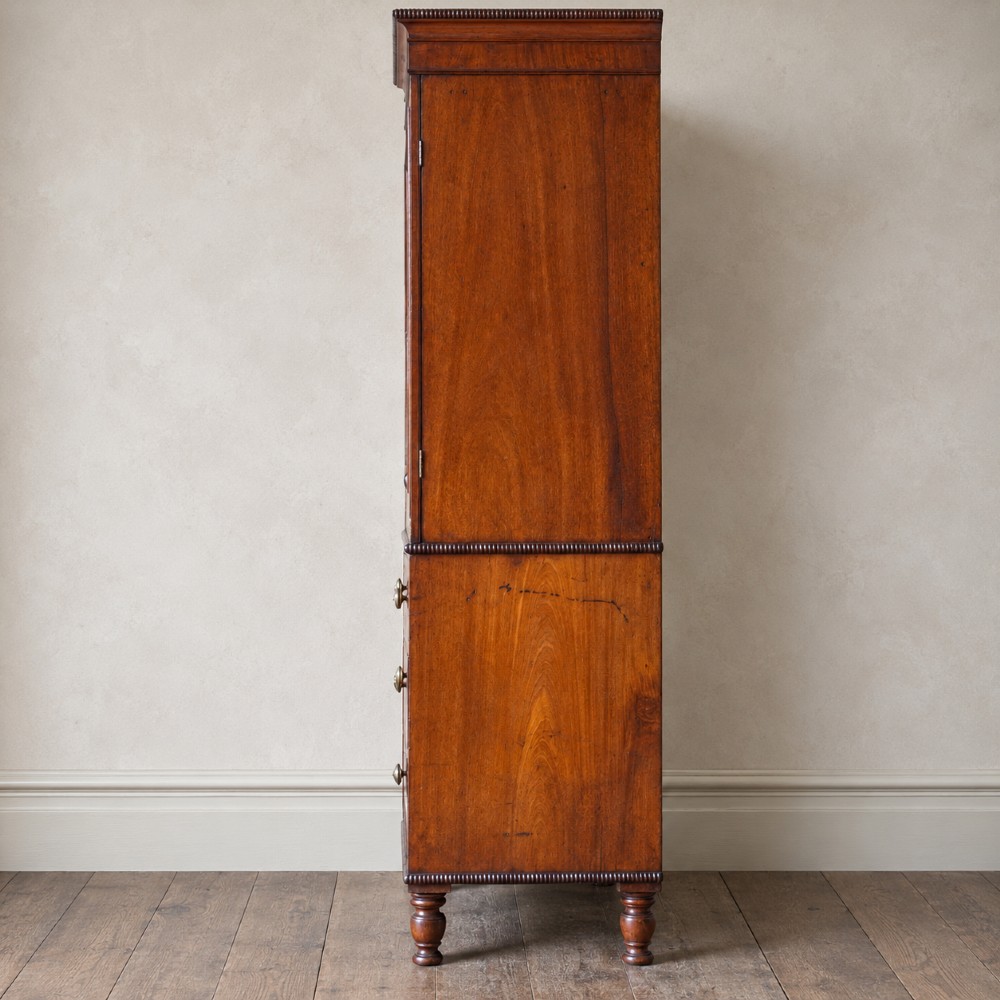 A Regency period flame mahogany linen press featuring a two-door upper cupboard above four drawers resting on turned legs. View IV