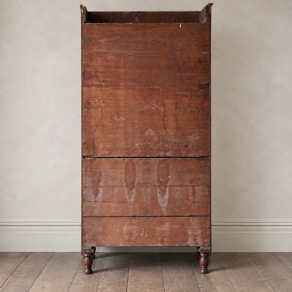 A Regency period flame mahogany linen press featuring a two-door upper cupboard above four drawers resting on turned legs. View V