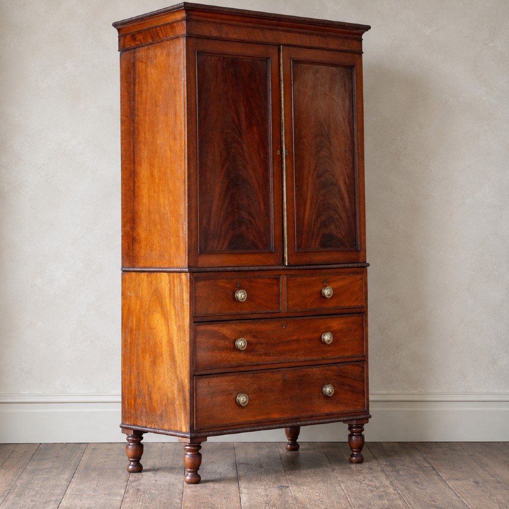 A Regency period flame mahogany linen press featuring a two-door upper cupboard above four drawers resting on turned legs. View VII