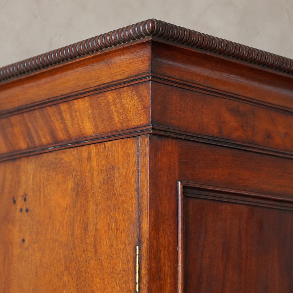 A Regency period flame mahogany linen press featuring a two-door upper cupboard above four drawers resting on turned legs. View VIII