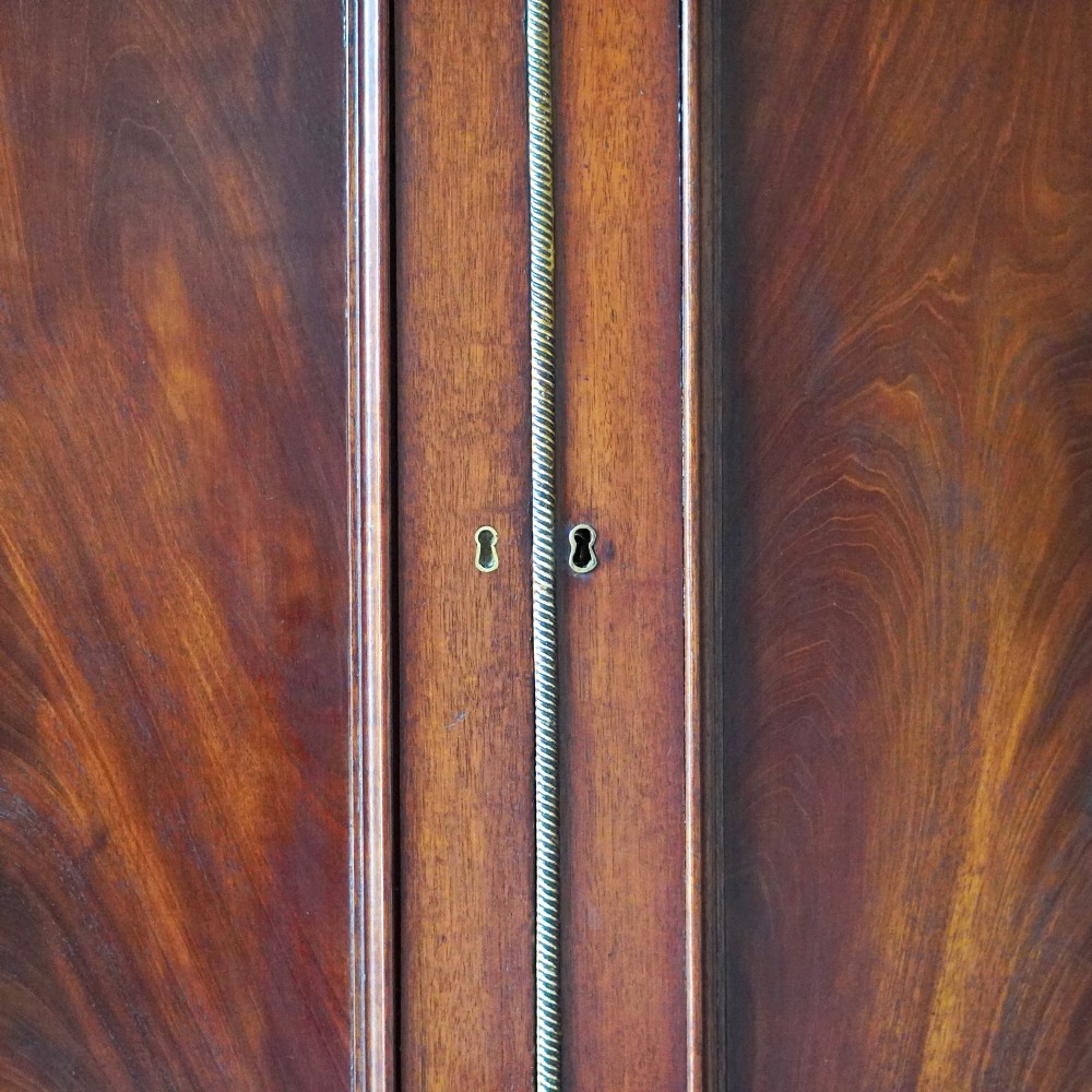 A Regency period flame mahogany linen press featuring a two-door upper cupboard above four drawers resting on turned legs. View IX