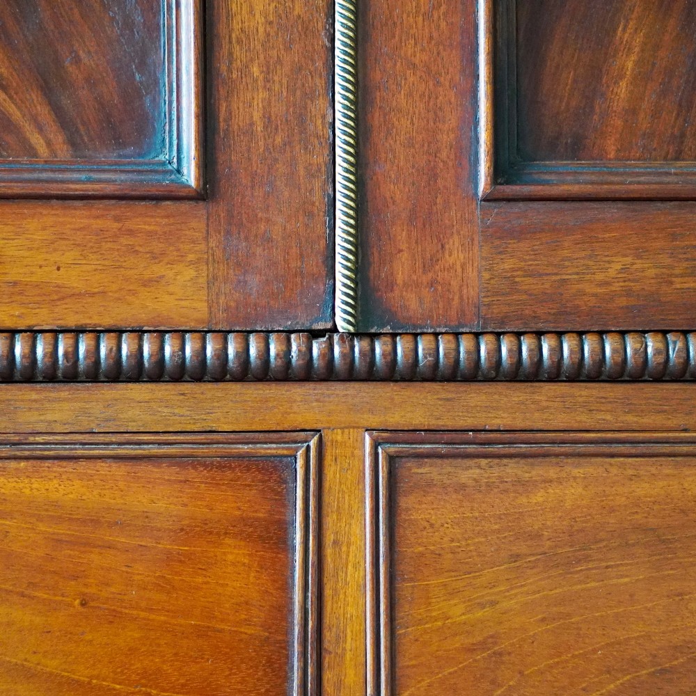 A Regency period flame mahogany linen press featuring a two-door upper cupboard above four drawers resting on turned legs. View XI