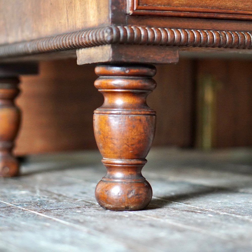A Regency period flame mahogany linen press featuring a two-door upper cupboard above four drawers resting on turned legs. View XII