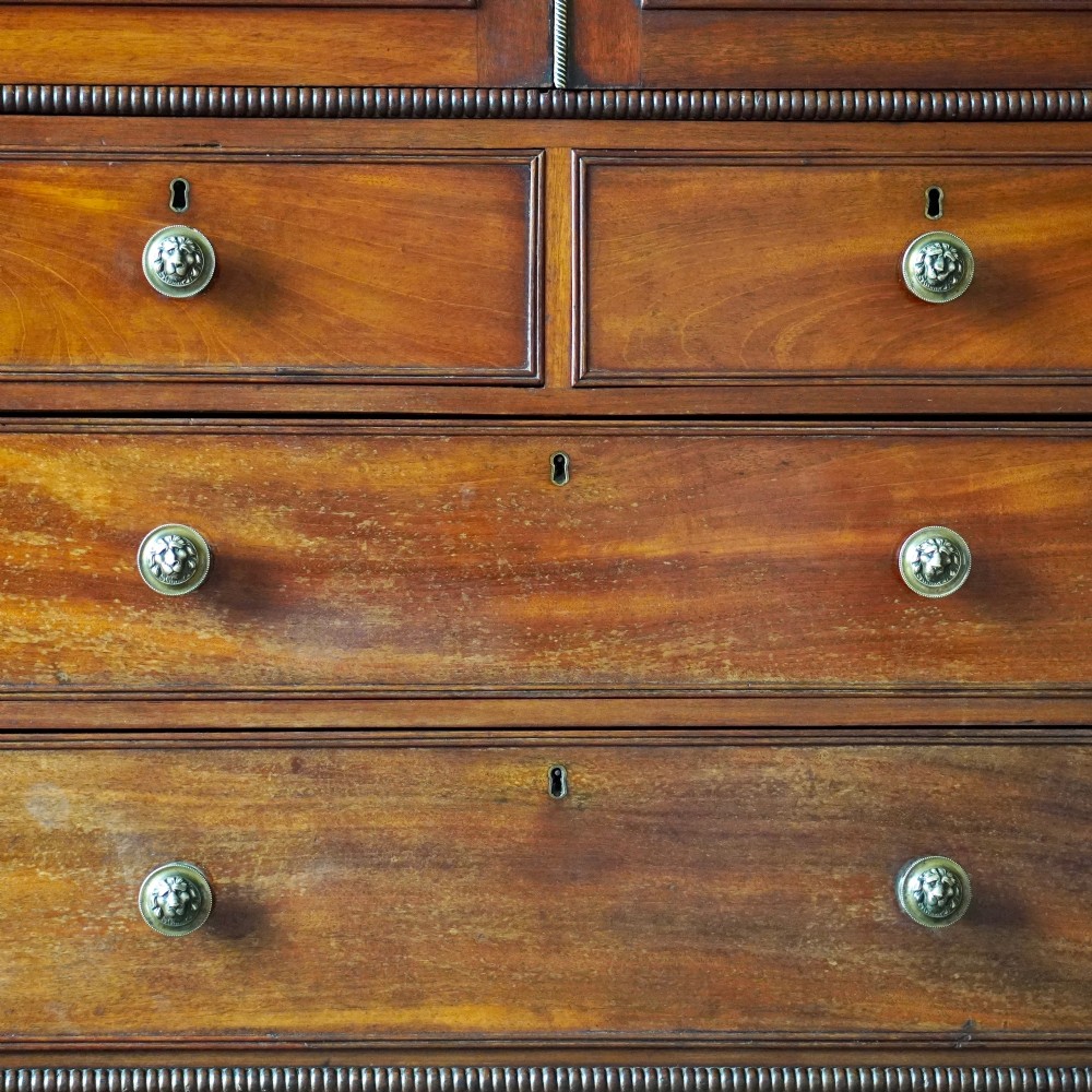A Regency period flame mahogany linen press featuring a two-door upper cupboard above four drawers resting on turned legs. View XV