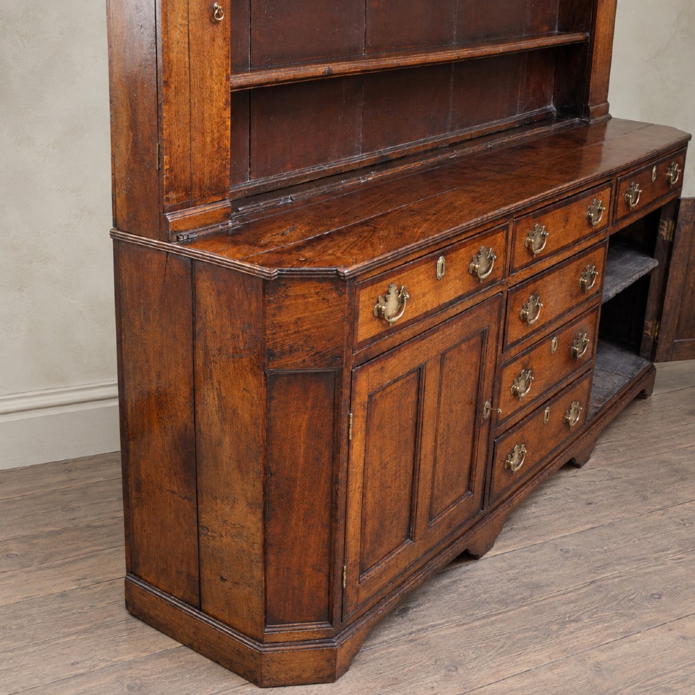 A George II dark oak dresser with a tall open plate rack above a sideboard featuring multiple drawers and twin cupboard doors. View III