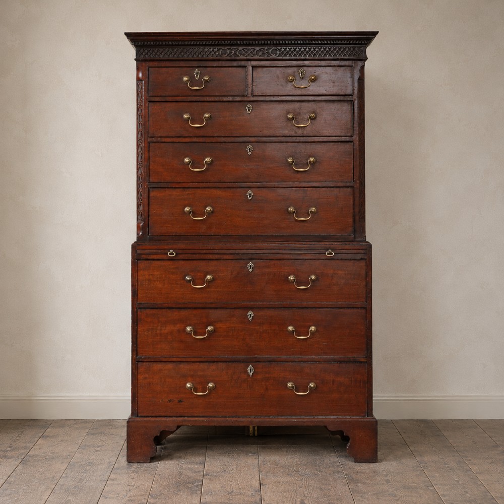 A George III mahogany chest on chest featuring two short over six long graduated drawers, a brushing slide, blind fretwork frieze, brass swan-neck handles, and bracket feet.