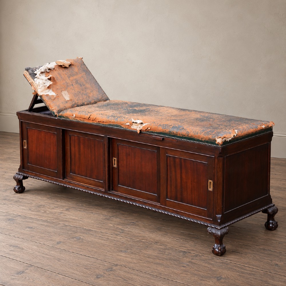 A long antique dark mahogany bench with four panelled cupboard doors, carved ball and claw feet, and a worn leather cushion top with a raised headrest. View II