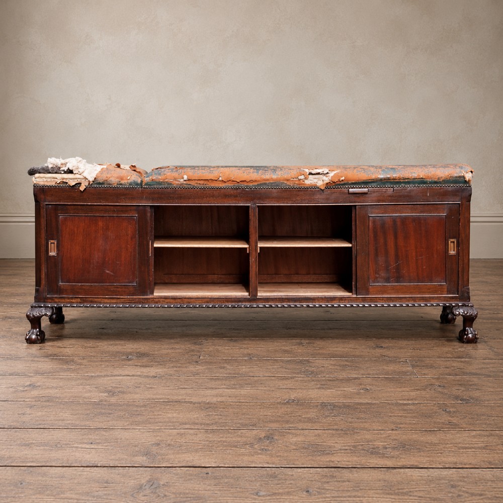 A long antique dark mahogany bench with four panelled cupboard doors, carved ball and claw feet, and a worn leather cushion top with a raised headrest. View III
