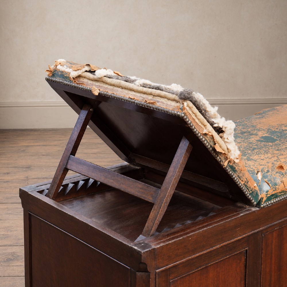A long antique dark mahogany bench with four panelled cupboard doors, carved ball and claw feet, and a worn leather cushion top with a raised headrest. View VI