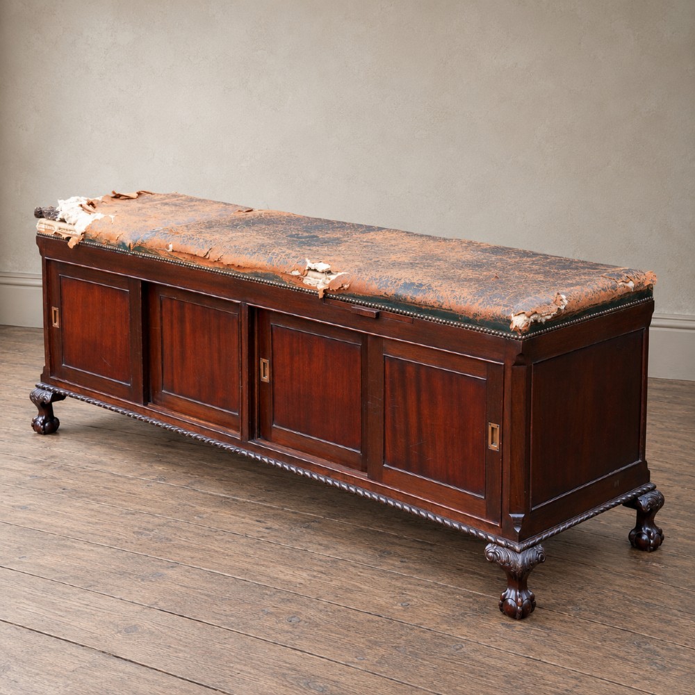 A long antique dark mahogany bench with four panelled cupboard doors, carved ball and claw feet, and a worn leather cushion top with a raised headrest. View VII