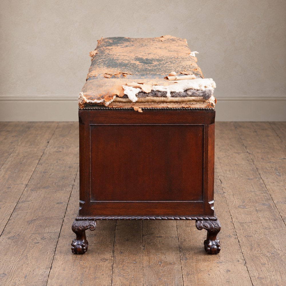 A long antique dark mahogany bench with four panelled cupboard doors, carved ball and claw feet, and a worn leather cushion top with a raised headrest. View VIII