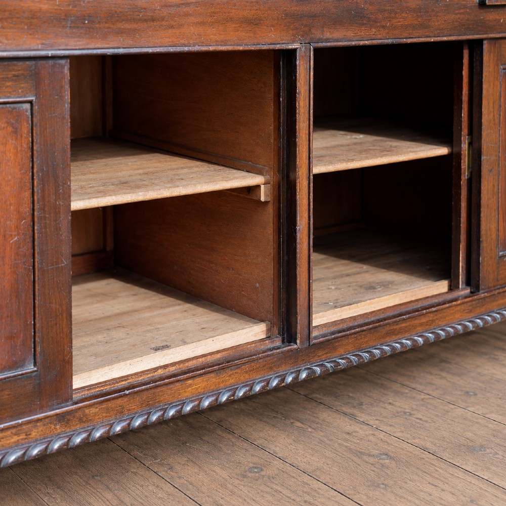 A long antique dark mahogany bench with four panelled cupboard doors, carved ball and claw feet, and a worn leather cushion top with a raised headrest. View IX