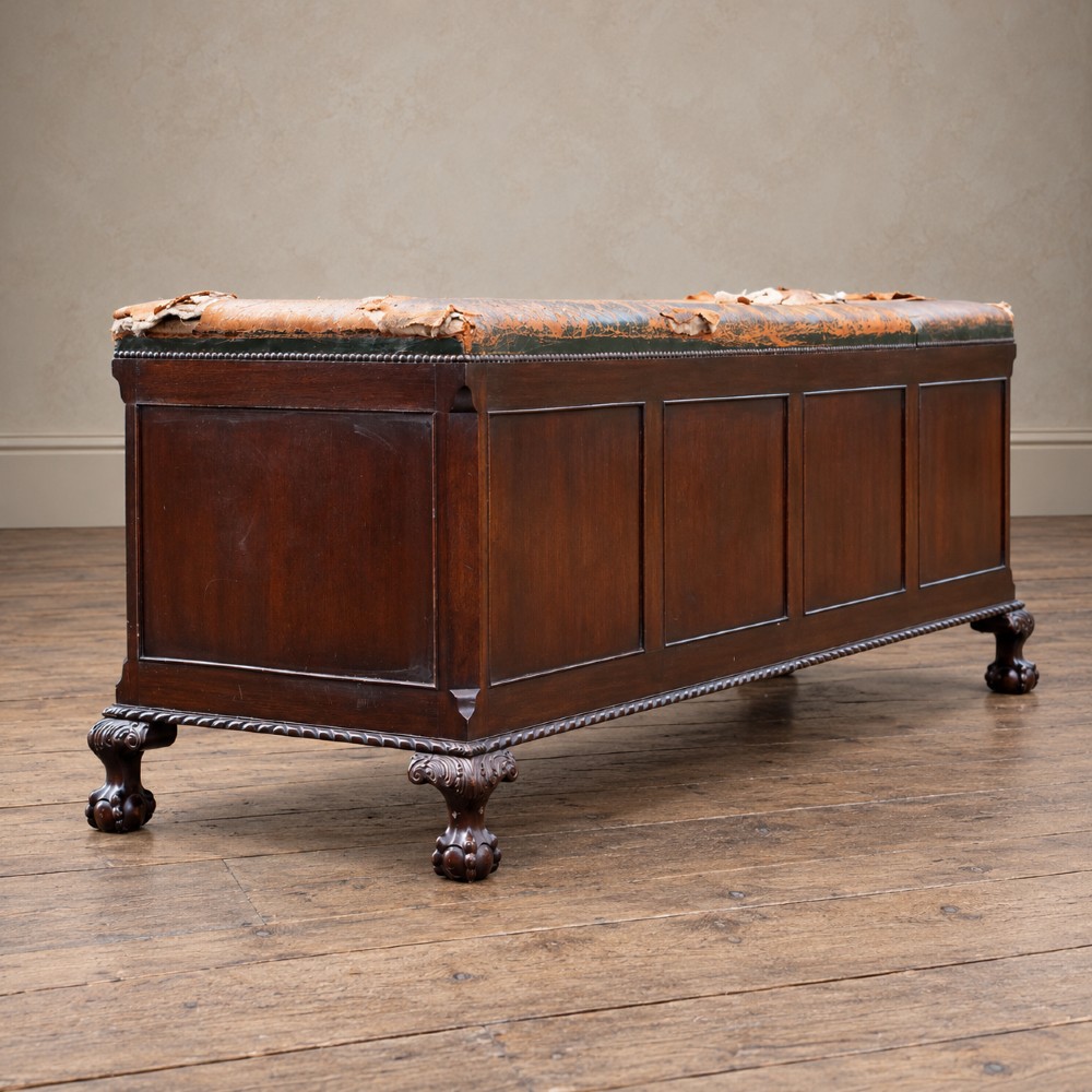 A long antique dark mahogany bench with four panelled cupboard doors, carved ball and claw feet, and a worn leather cushion top with a raised headrest. View X