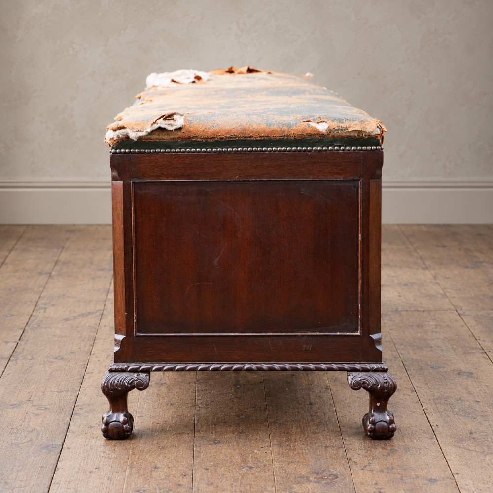 A long antique dark mahogany bench with four panelled cupboard doors, carved ball and claw feet, and a worn leather cushion top with a raised headrest. View XI