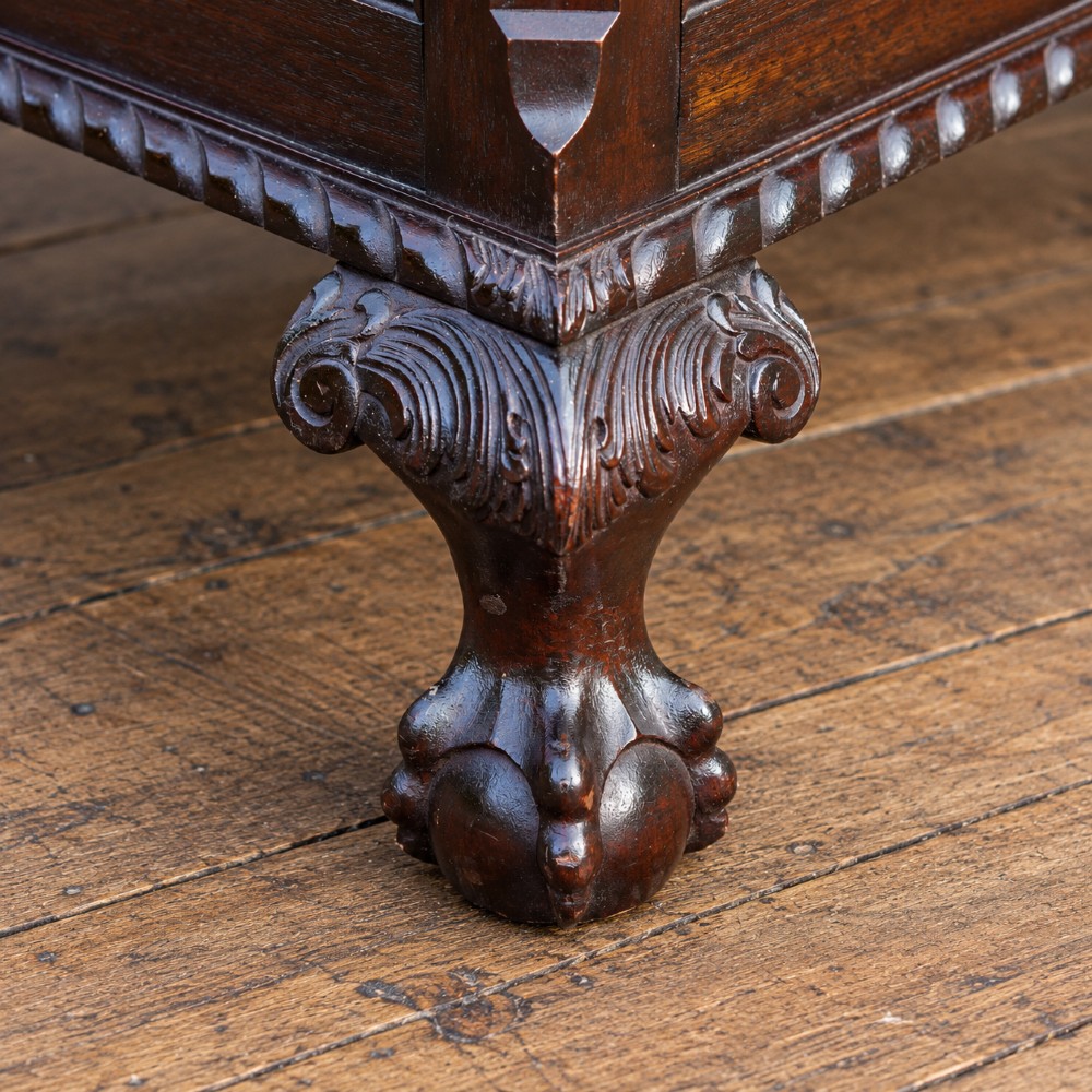 A long antique dark mahogany bench with four panelled cupboard doors, carved ball and claw feet, and a worn leather cushion top with a raised headrest. View XII