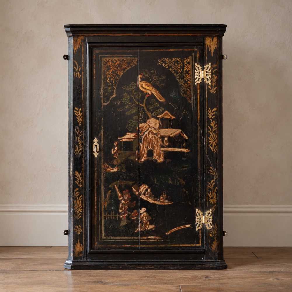 An 18th-century black japanned single-door wall corner cupboard featuring hand-painted gold Chinoiserie figures, architectural motifs, and brass butterfly hinges.