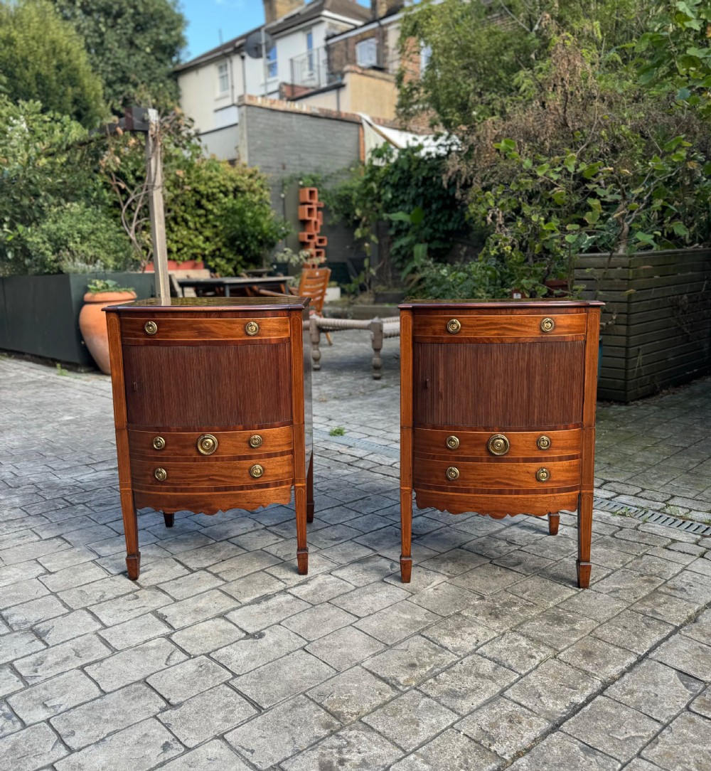 A pair of George III mahogany bedside cabinets featuring tambour slatted doors, brass ring handles, satinwood inlay, and tapered legs.