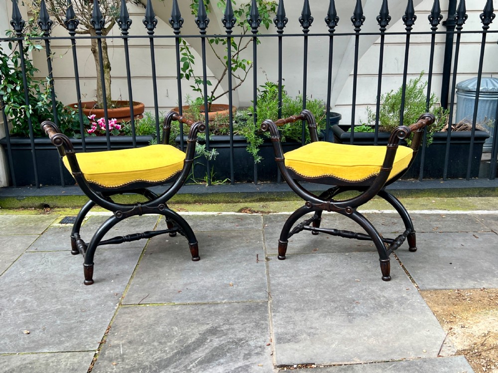 A pair of Regency period ebonised oak window seats featuring X-frame curule bases, scroll arms, and button-tufted yellow upholstery. View II