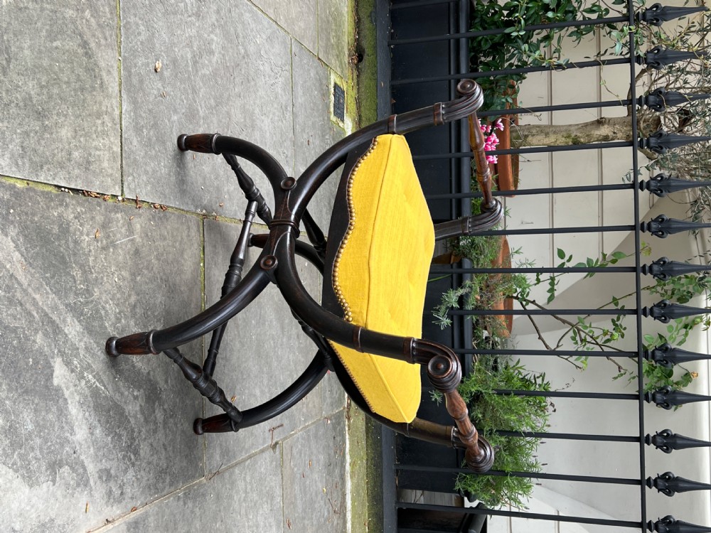 A pair of Regency period ebonised oak window seats featuring X-frame curule bases, scroll arms, and button-tufted yellow upholstery. View III