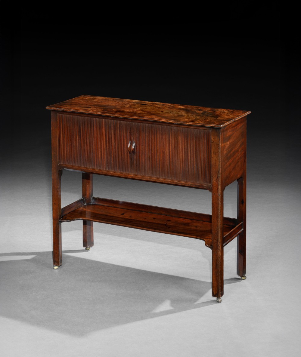 A George III mahogany cabinet featuring a tambour shutter door enclosure, a lower open tier with a shaped apron, and straight legs supported by brass castors. View III