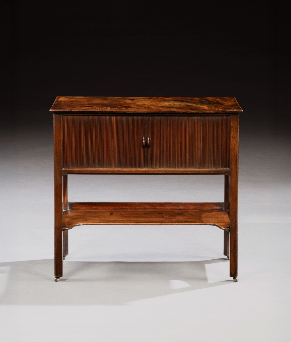 A George III mahogany cabinet featuring a tambour shutter door enclosure, a lower open tier with a shaped apron, and straight legs supported by brass castors. View II