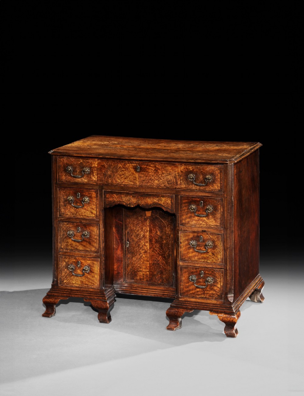 A George II fiddleback walnut kneehole desk featuring a central recessed cupboard, upper long drawer, six side drawers, and brass handles. View II