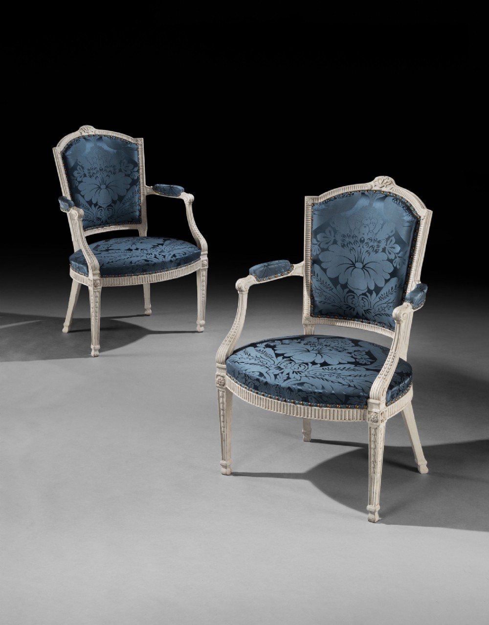 A pair of George III style cream-painted armchairs with fluted legs and blue floral damask upholstery.