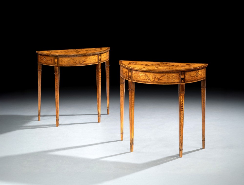A pair of George III period semi-circular satinwood side tables featuring inlaid marquetry tops and square tapered legs.