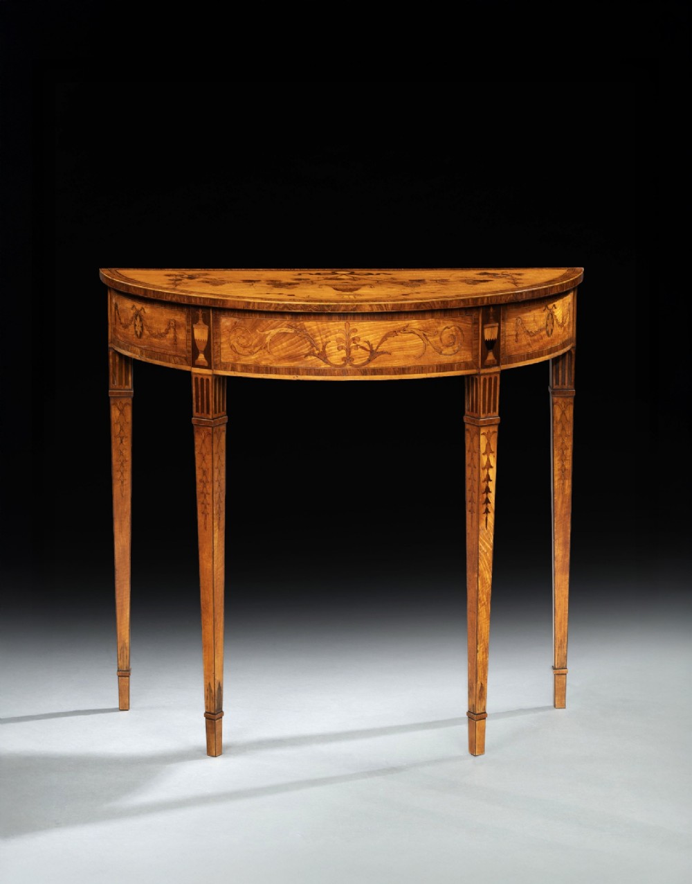A pair of George III period semi-circular satinwood side tables featuring inlaid marquetry tops and square tapered legs. View II