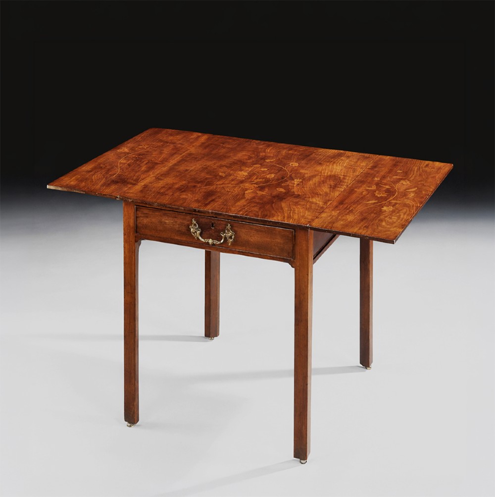 A George III mahogany Pembroke table featuring foliate inlay on the top, two hinged leaves, one drawer with a brass handle, and four square tapered legs on castors.